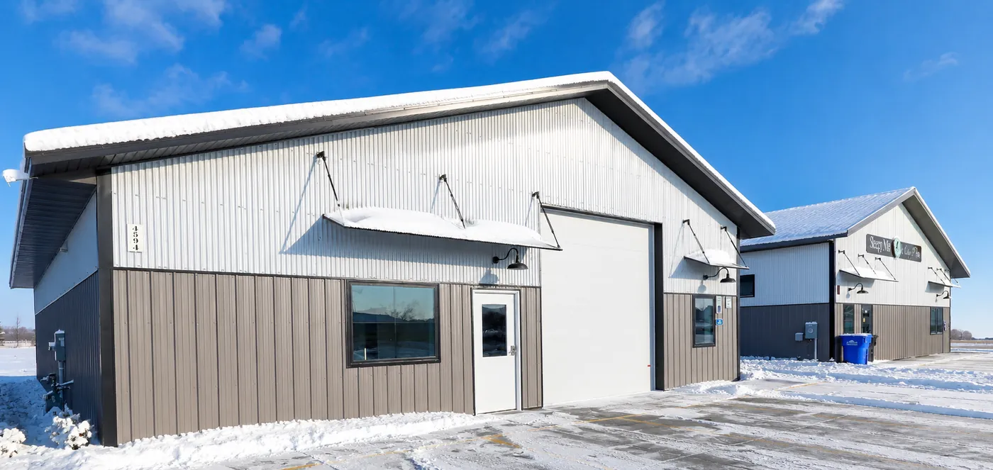 Completed commercial post-frame building with metal siding, standing in a snowy North Dakota winter landscape under a clear blue sky