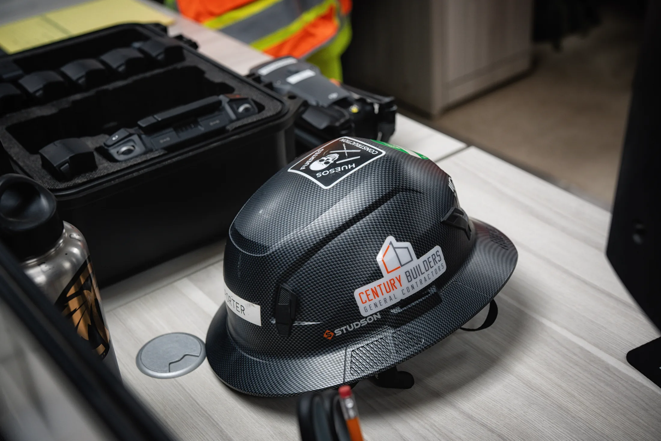 Century Builders hard hat on a job-site table beside field equipment